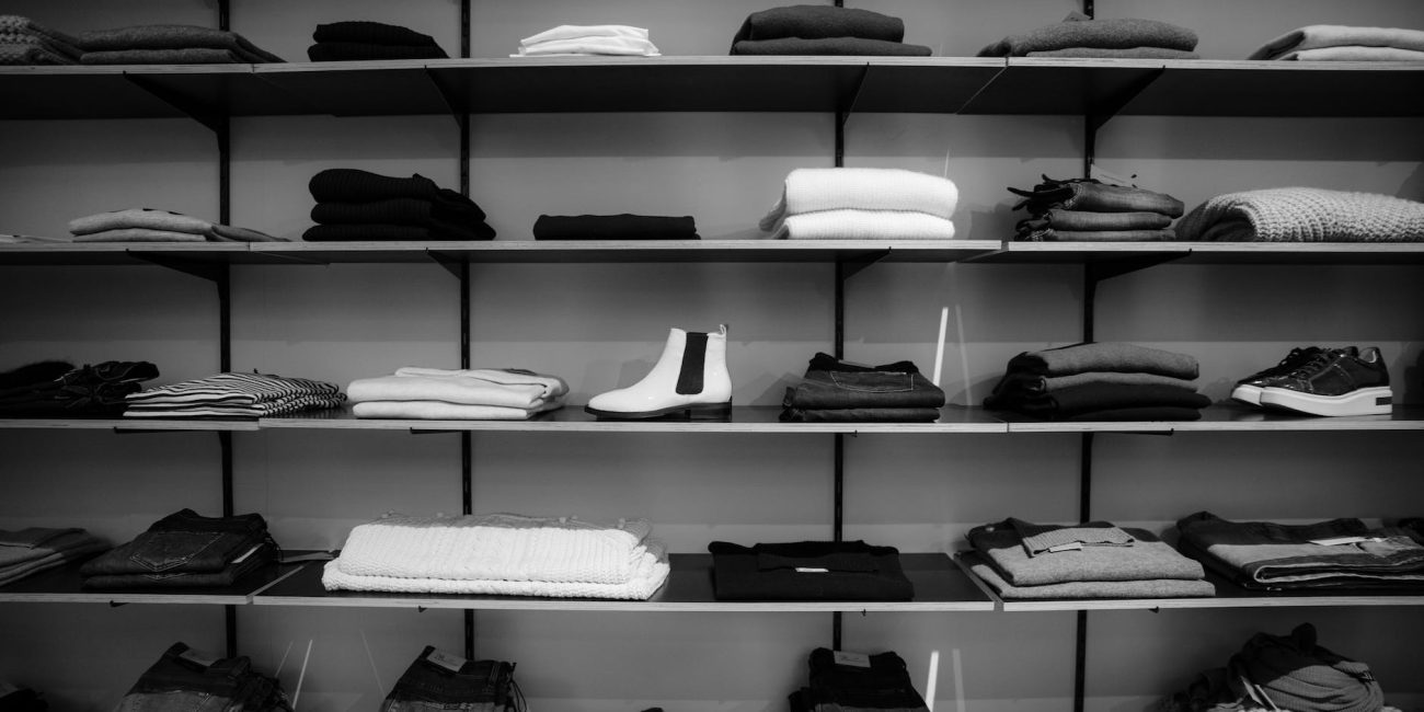 grayscale photography of assorted apparels on shelf rack